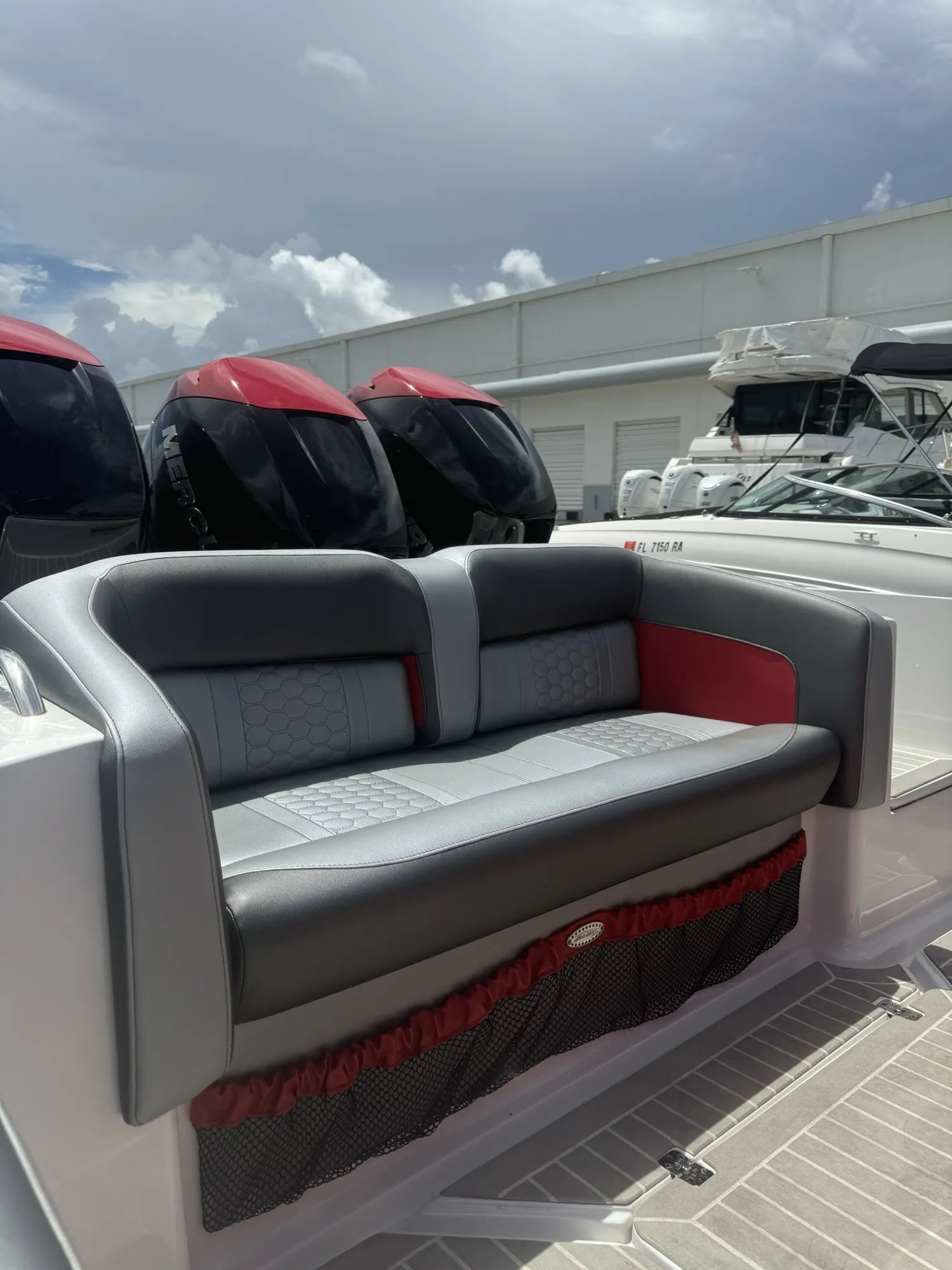 Grey and red aft bench seating with hexagon quilting and a red-trimmed netted storage pocket, on a triple-outboard center console