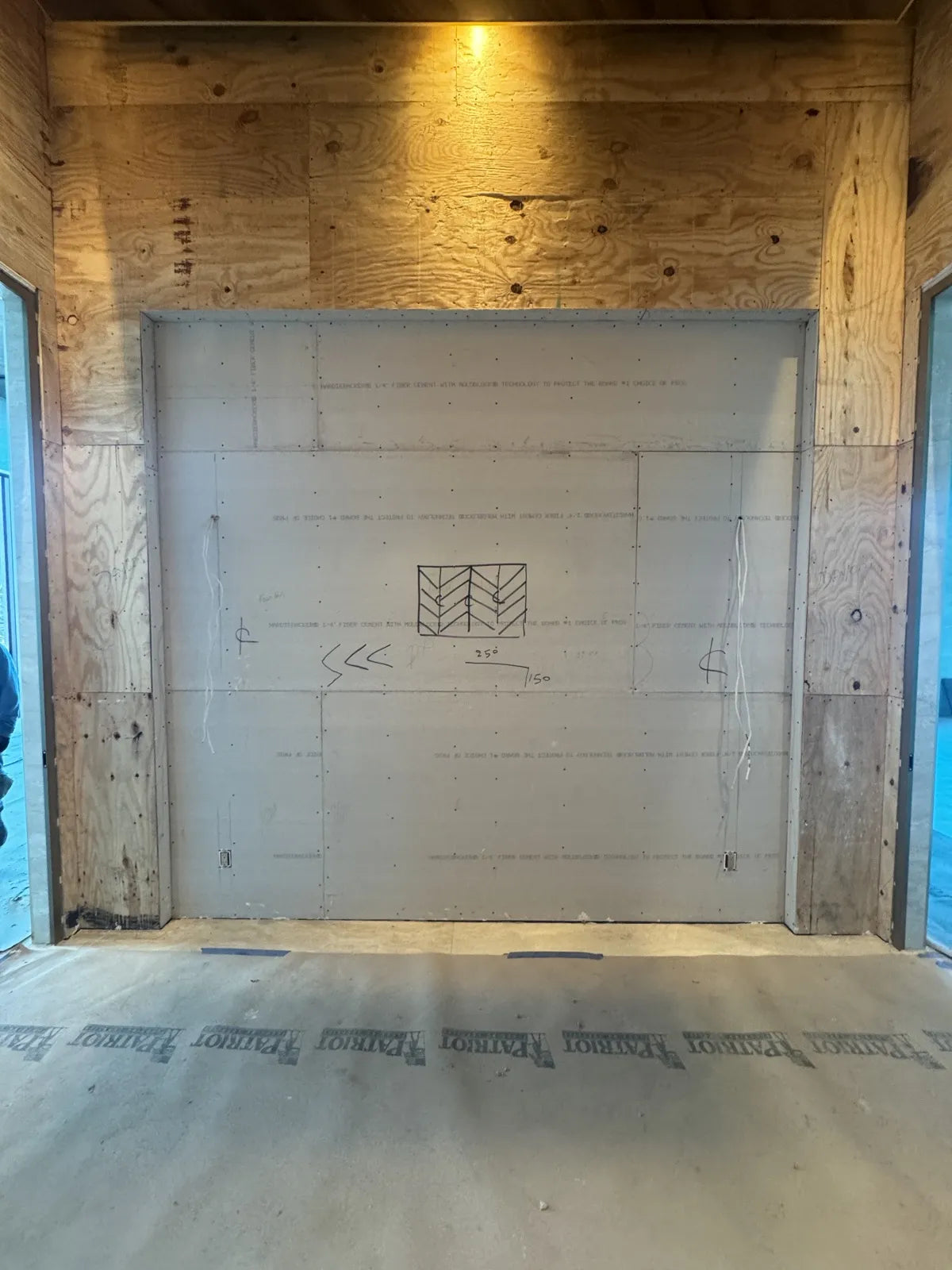 Bare fiber-cement board over plywood framing, with the chevron panel layout drawn on it in pencil and two cable drops hanging