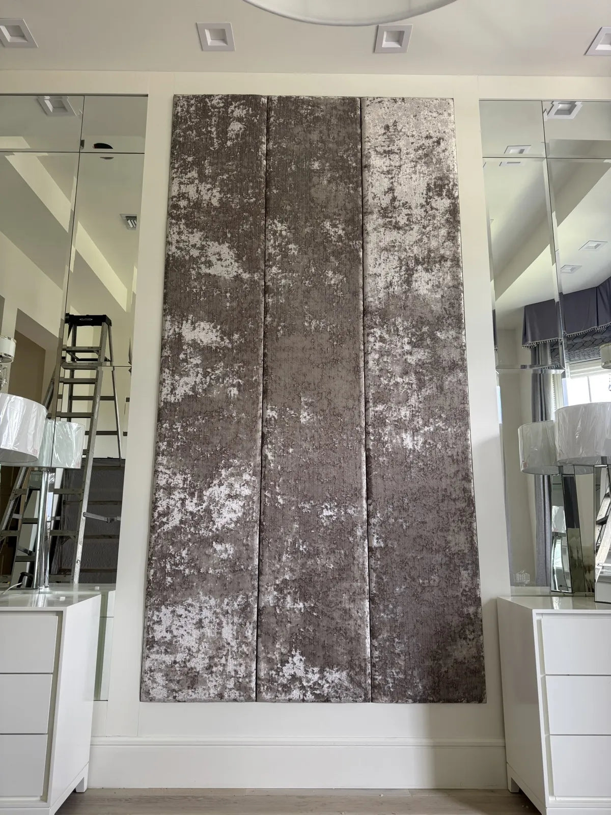 The same wall finished as three full-height upholstered panels in a distressed silver velvet, running floor to ceiling between the mirrors
