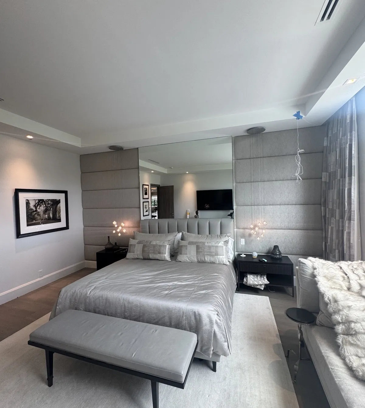 Bedroom with a full upholstered soft wall in grey textured fabric behind the bed, running floor to ceiling either side of a mirror