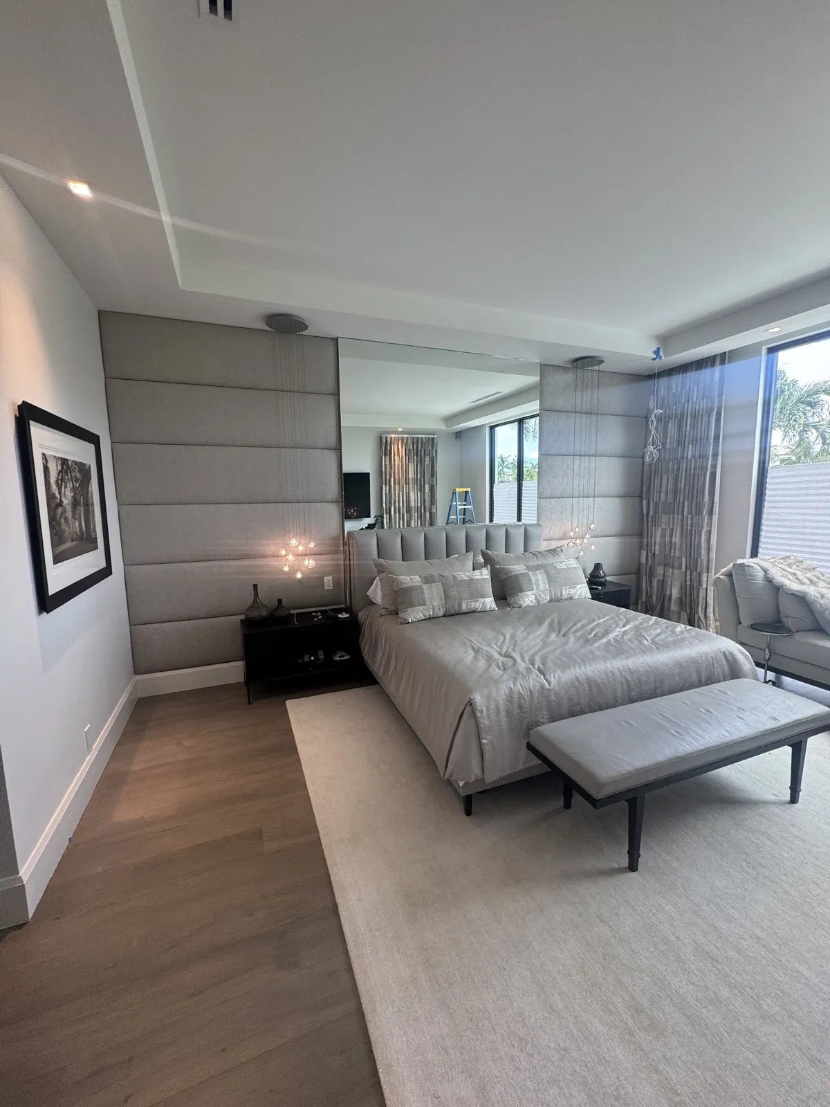 Wide view of a bedroom with upholstered wall panels flanking a full-height mirror, seen from the doorway