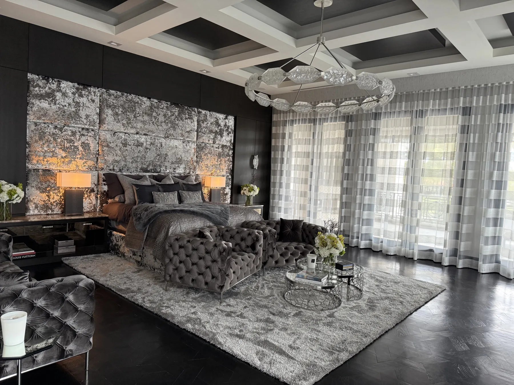 Bedroom with a full-height upholstered headboard wall in distressed silver and charcoal fabric, set into black joinery under a coffered ceiling