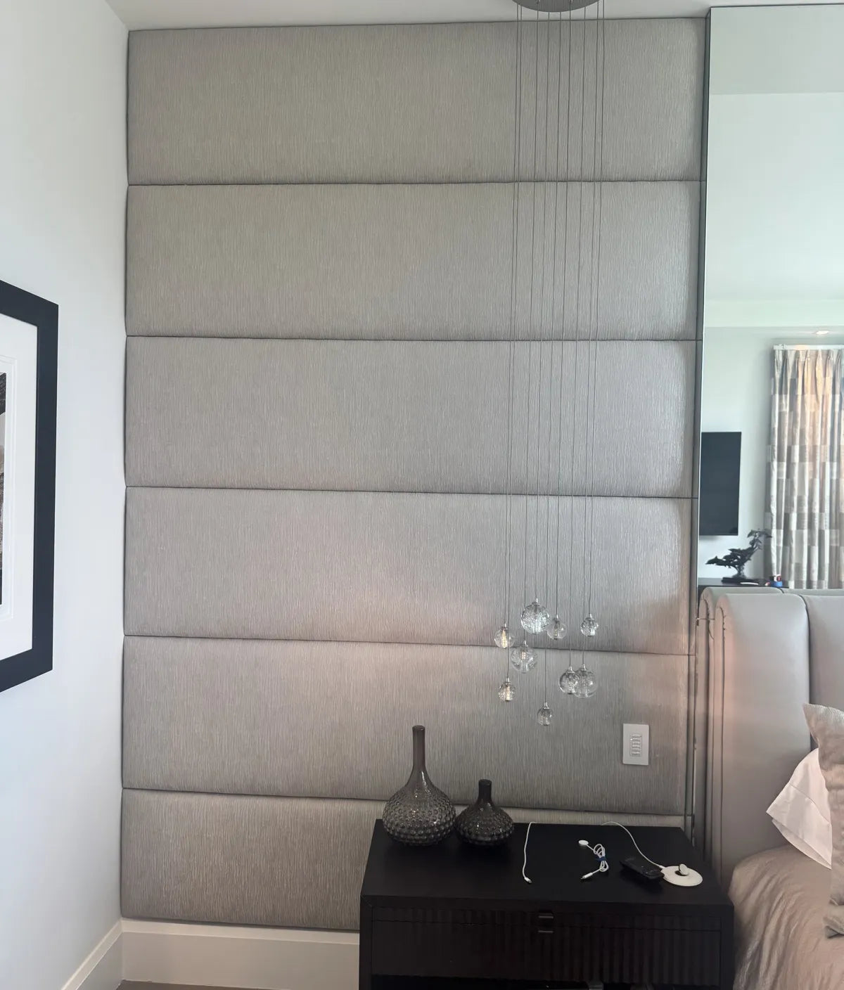 Close view of horizontal upholstered wall panels in grey textured fabric, showing the seams between panels and the return into the mirror