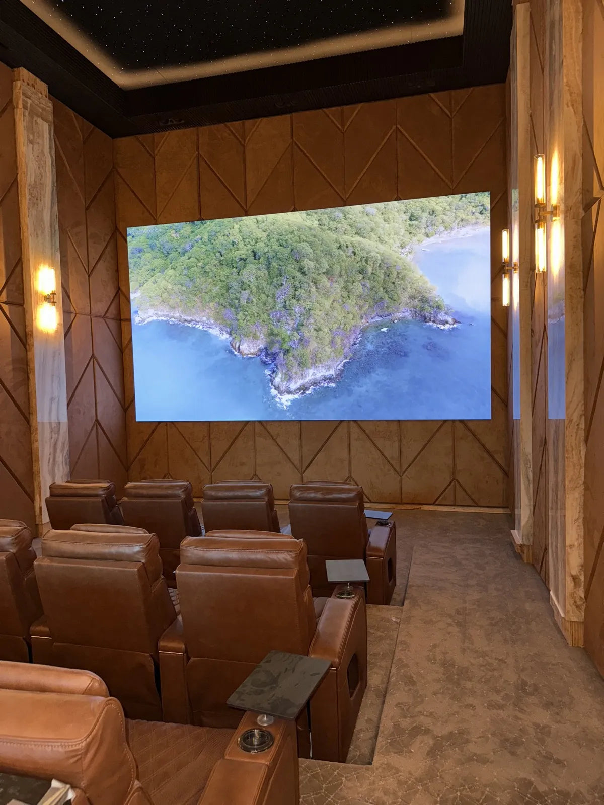 Home theater seen from the back row, upholstered chevron wall panels flanking the screen and continuing down the side walls