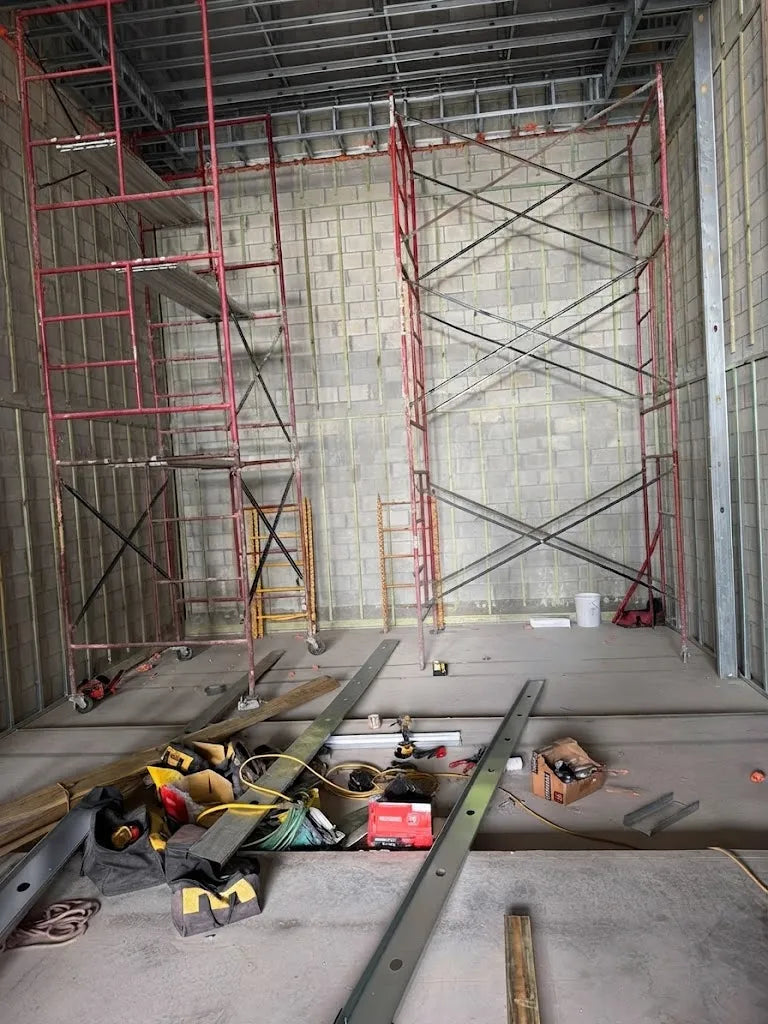The theater room as a bare shell: block wall, steel stud framing, scaffolding and tools on a concrete floor