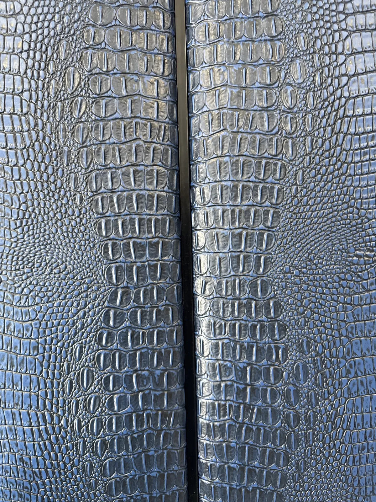 Close view of two navy crocodile-embossed upholstered panels meeting at a tight vertical seam